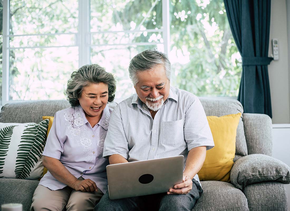 General Medicare - Senior Couple Laughing While Sitting on the Sofa in a Bright Living Room and Using Laptop to Review Their Medicare Options