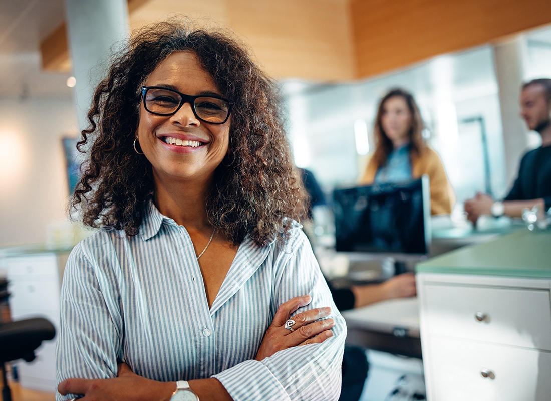 Business Insurance - Closeup Portrait of a Cheerful Middle Aged Business Woman Standing in an Office with Employees Working in the Background