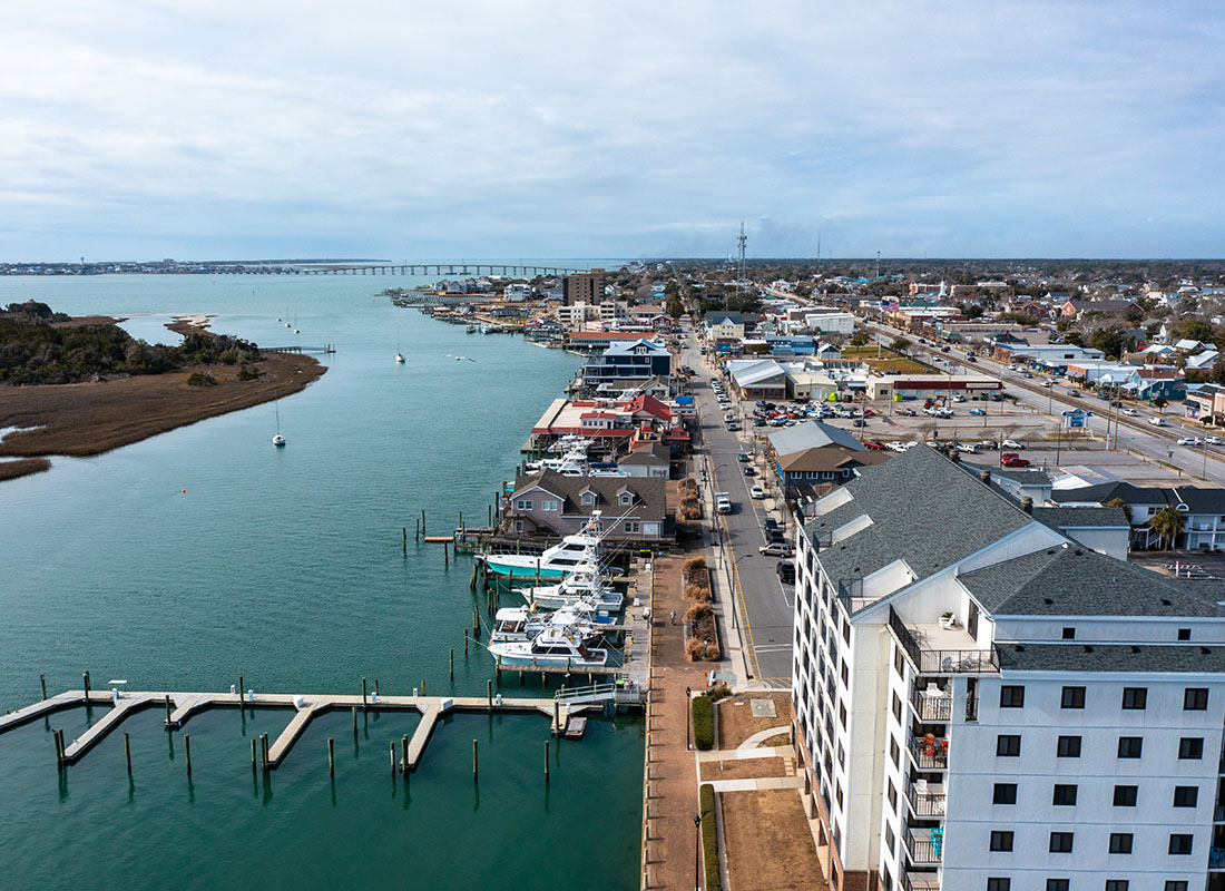 Morehead City, NC - Aerial View of Buildings and Homes Next to a Bright Blue River with Boats on the Dock in Morehead City North Carolina