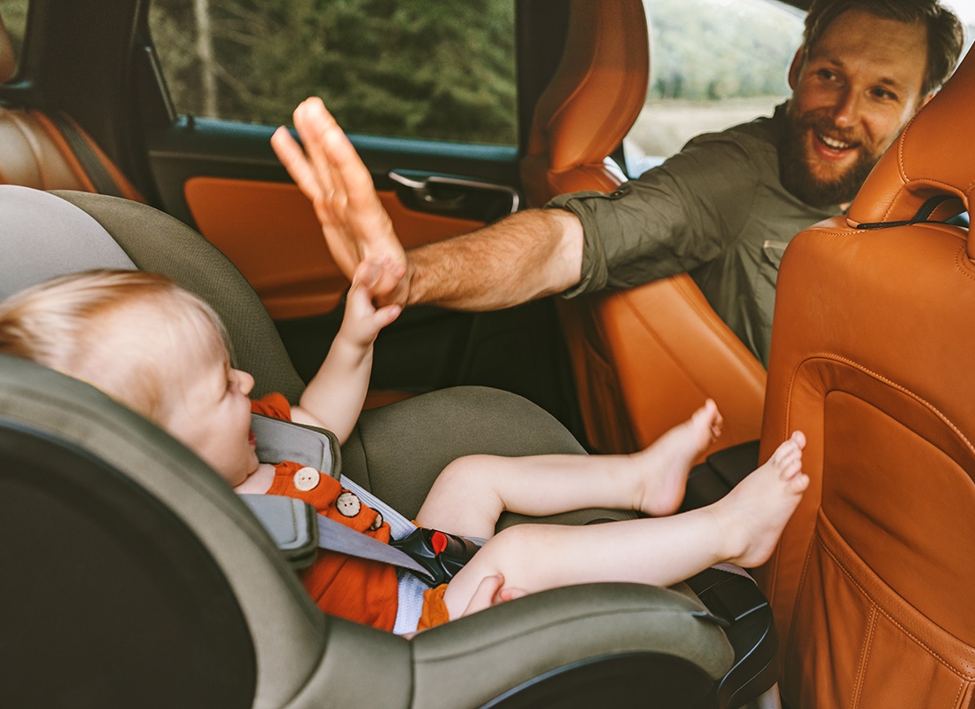Personal Insurance - Portrait of a Smiling Father Sitting in the Front Seat of a Car Giving his Toddler in a Child Seat High Five